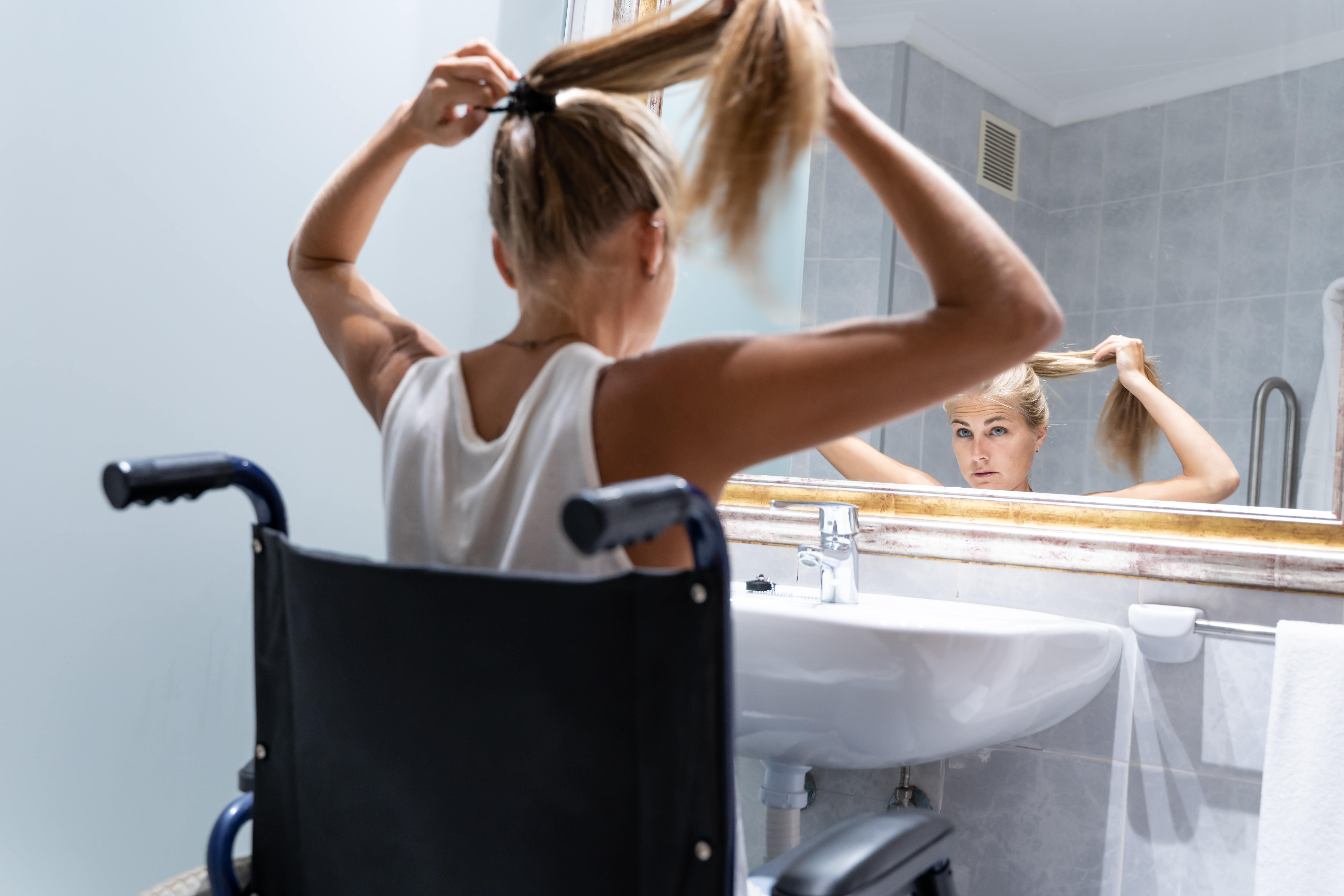 Young woman in a wheelchair using an accessible bathroom in Hampshrie and West Sussex, featuring a walk-in shower and mobility-friendly wash basin.